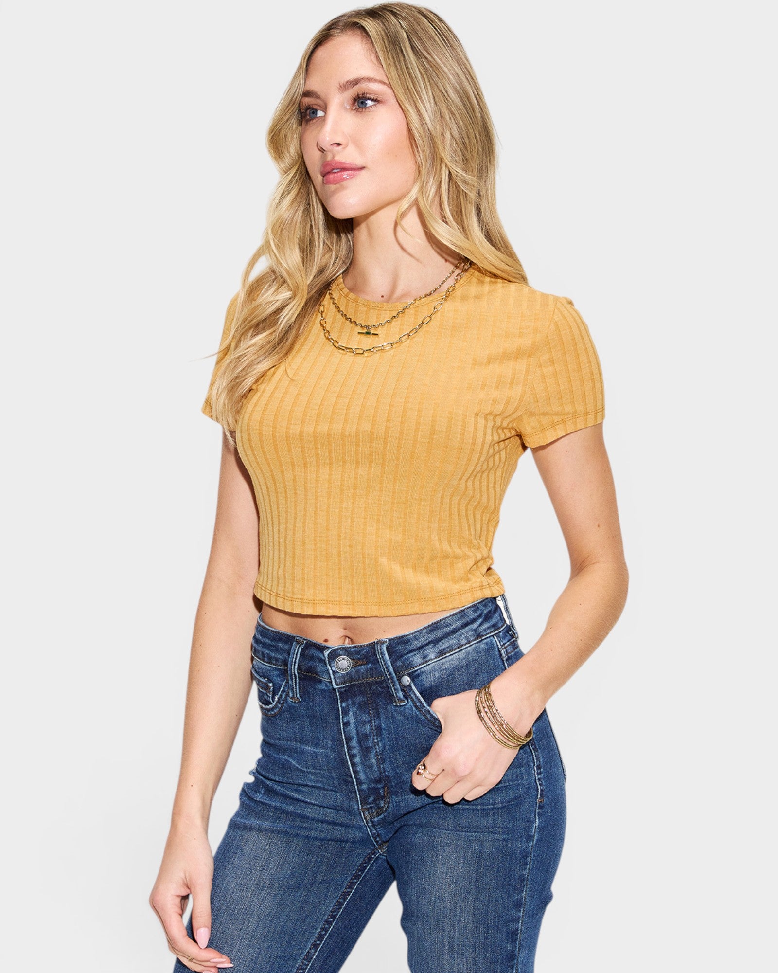 Woman wearing a yellow top and blue jeans on a light gray background