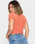 Woman wearing a coral ribbed top and blue jeans on a white background