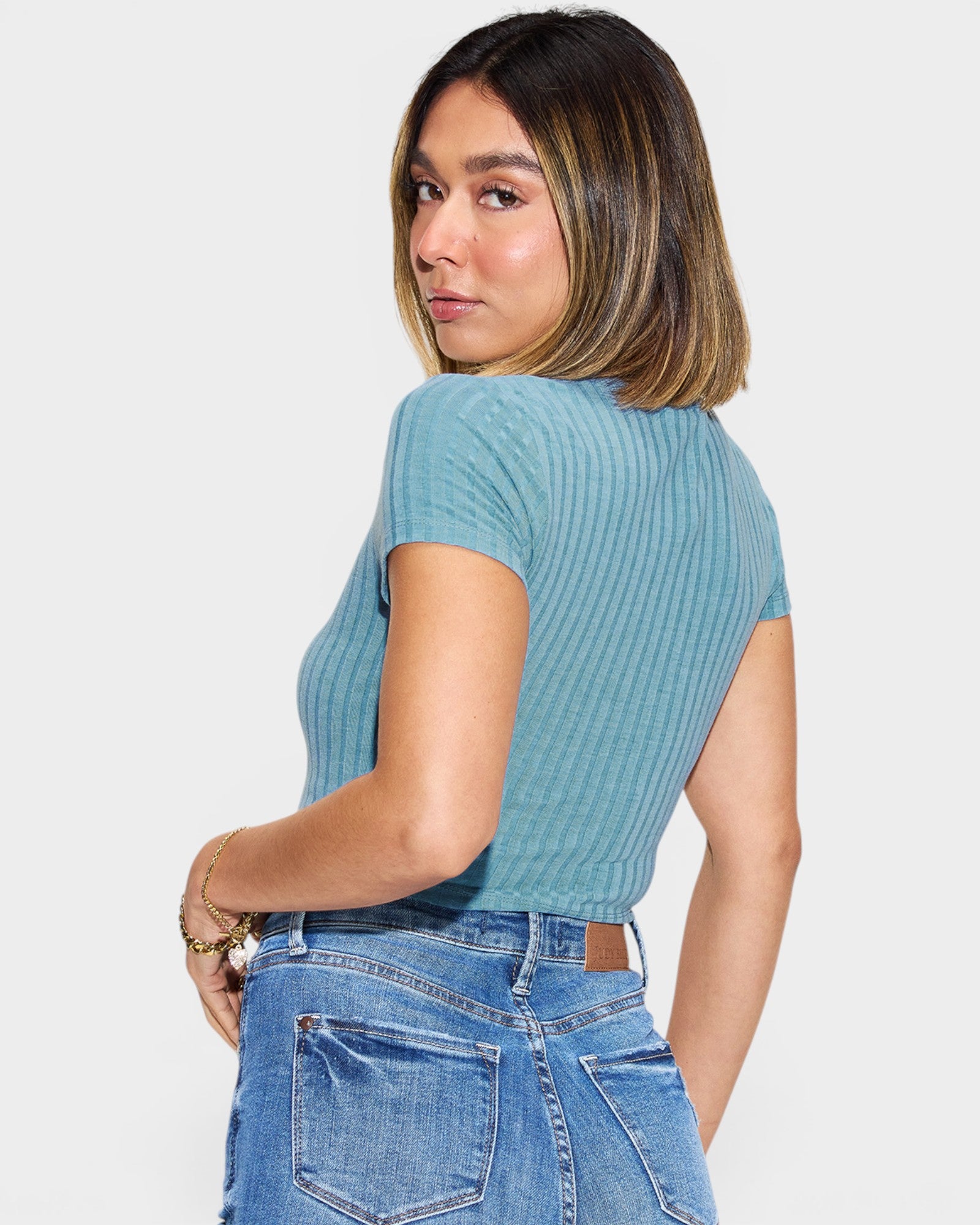 Woman wearing a blue ribbed top and jeans on a plain background