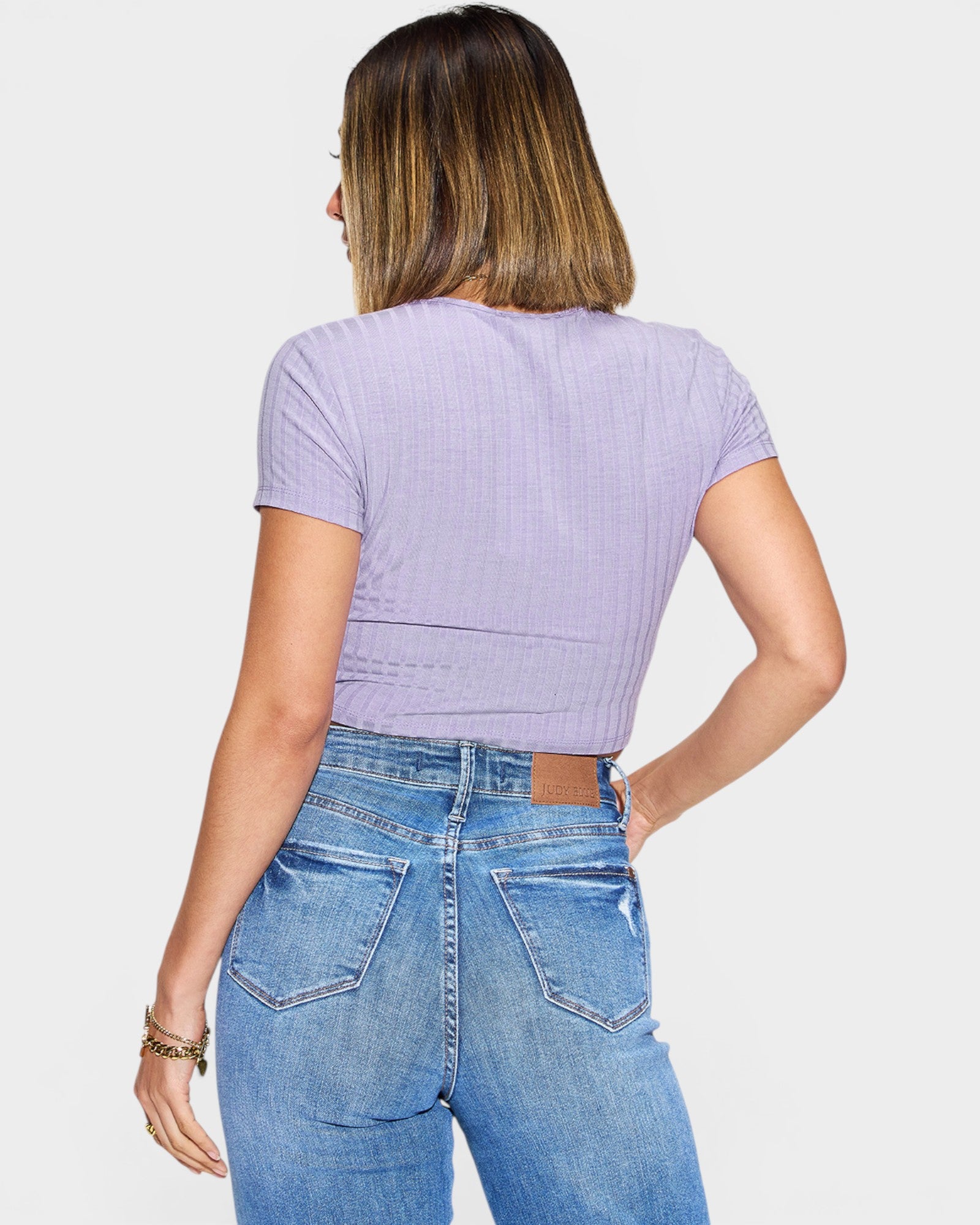 Person wearing a purple ribbed crop top and blue jeans on a white background
