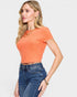 Woman wearing an orange ribbed top and blue jeans on a light gray background