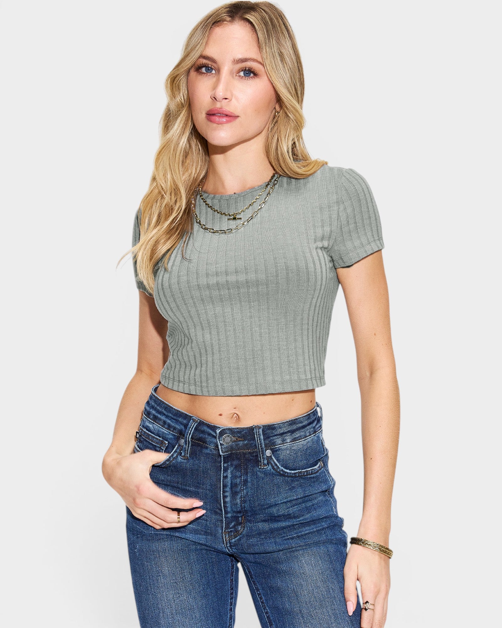 Woman wearing a green ribbed crop top and blue jeans on a white background
