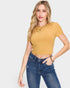 Woman wearing a mustard yellow ribbed crop top and blue jeans on a white background