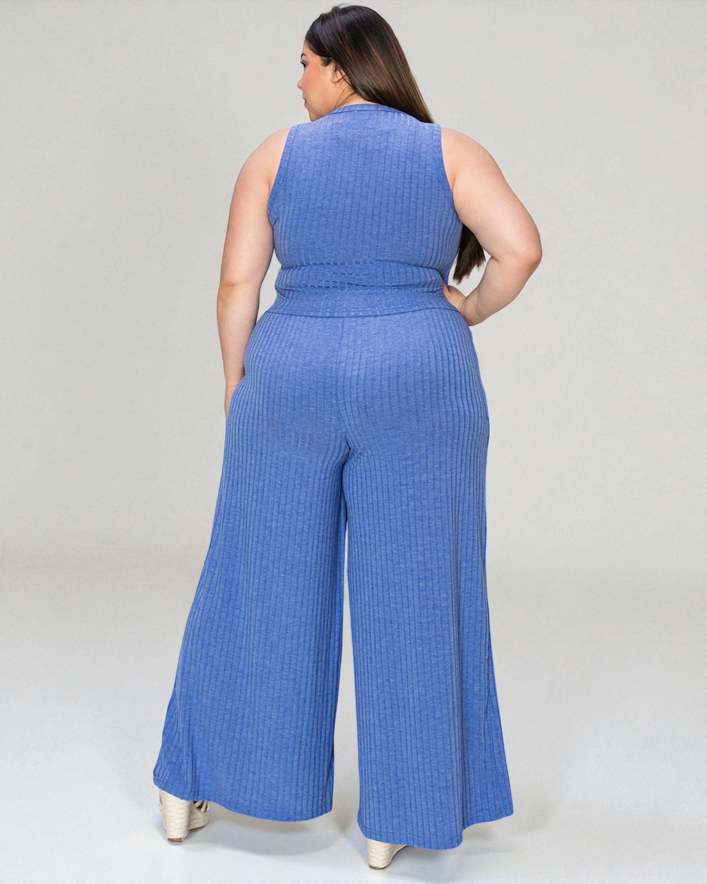 Woman wearing a blue ribbed jumpsuit on a plain background