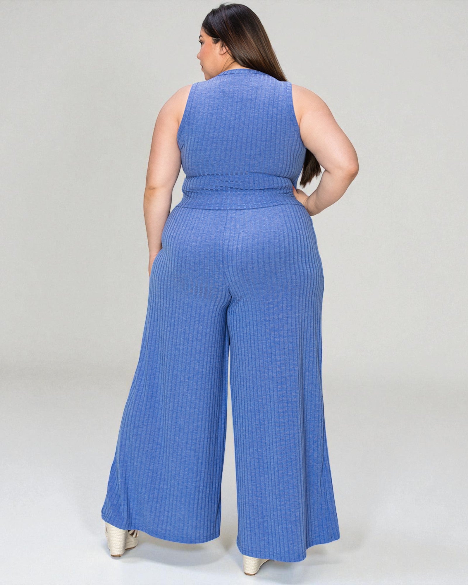 Woman wearing a blue ribbed jumpsuit on a plain background