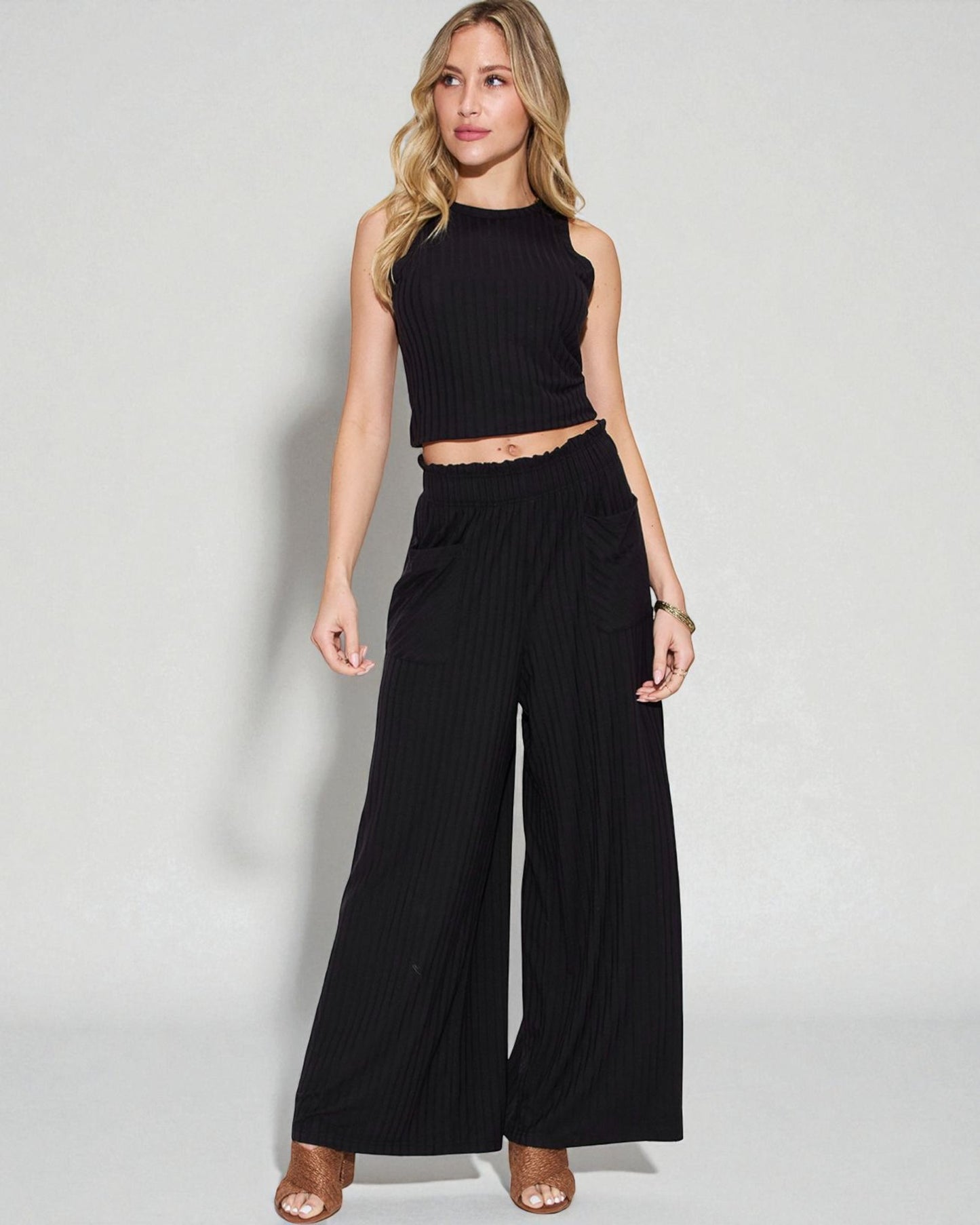 Woman wearing a black sleeveless top and wide-leg pants on a white background