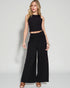 Woman wearing a black sleeveless top and wide-leg pants on a white background