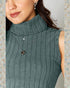 Woman wearing a green turtleneck sweater with a necklace and earrings against a neutral background