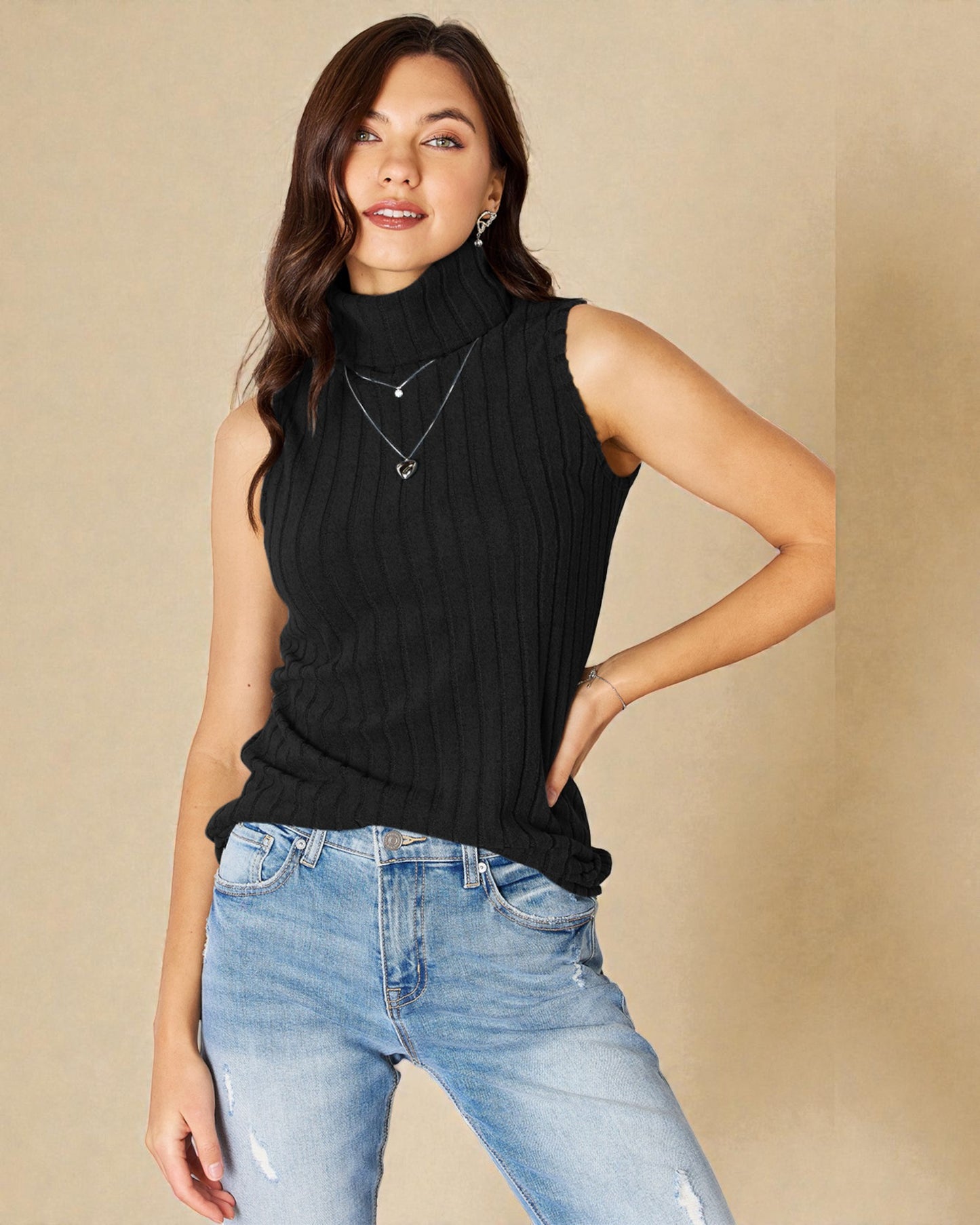 Woman wearing a black sleeveless top and blue jeans against a beige background