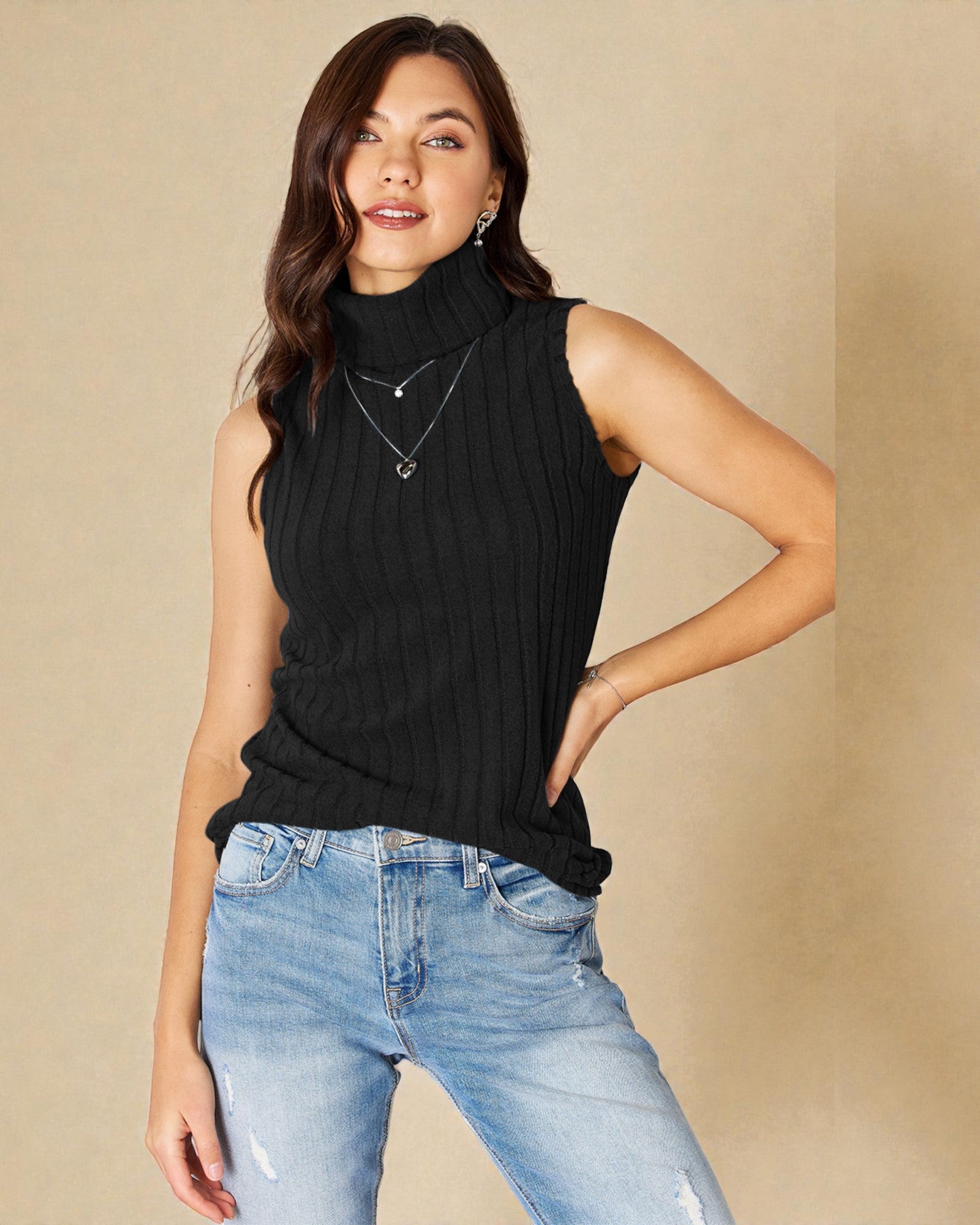 Woman wearing a black sleeveless top and blue jeans against a beige background