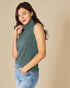 Woman wearing a green sleeveless ribbed sweater and blue jeans against a beige background