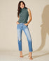 Woman wearing a green sleeveless sweater and blue jeans on a beige background