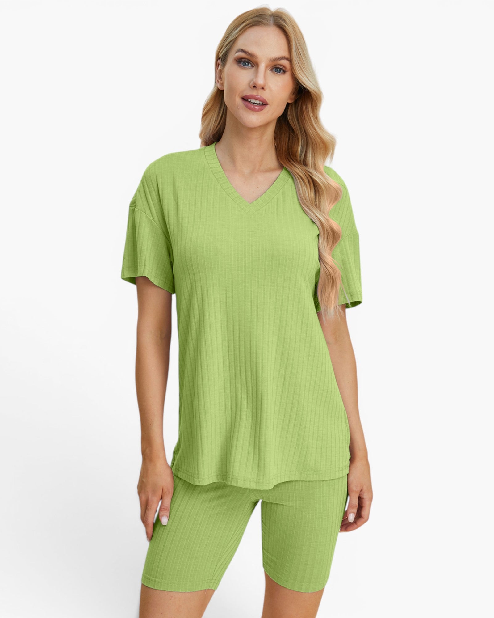 A woman modeling a matching lime green ribbed two-piece loungewear set consisting of a short-sleeve V-neck top and fitted biker shorts, against a plain white studio background.