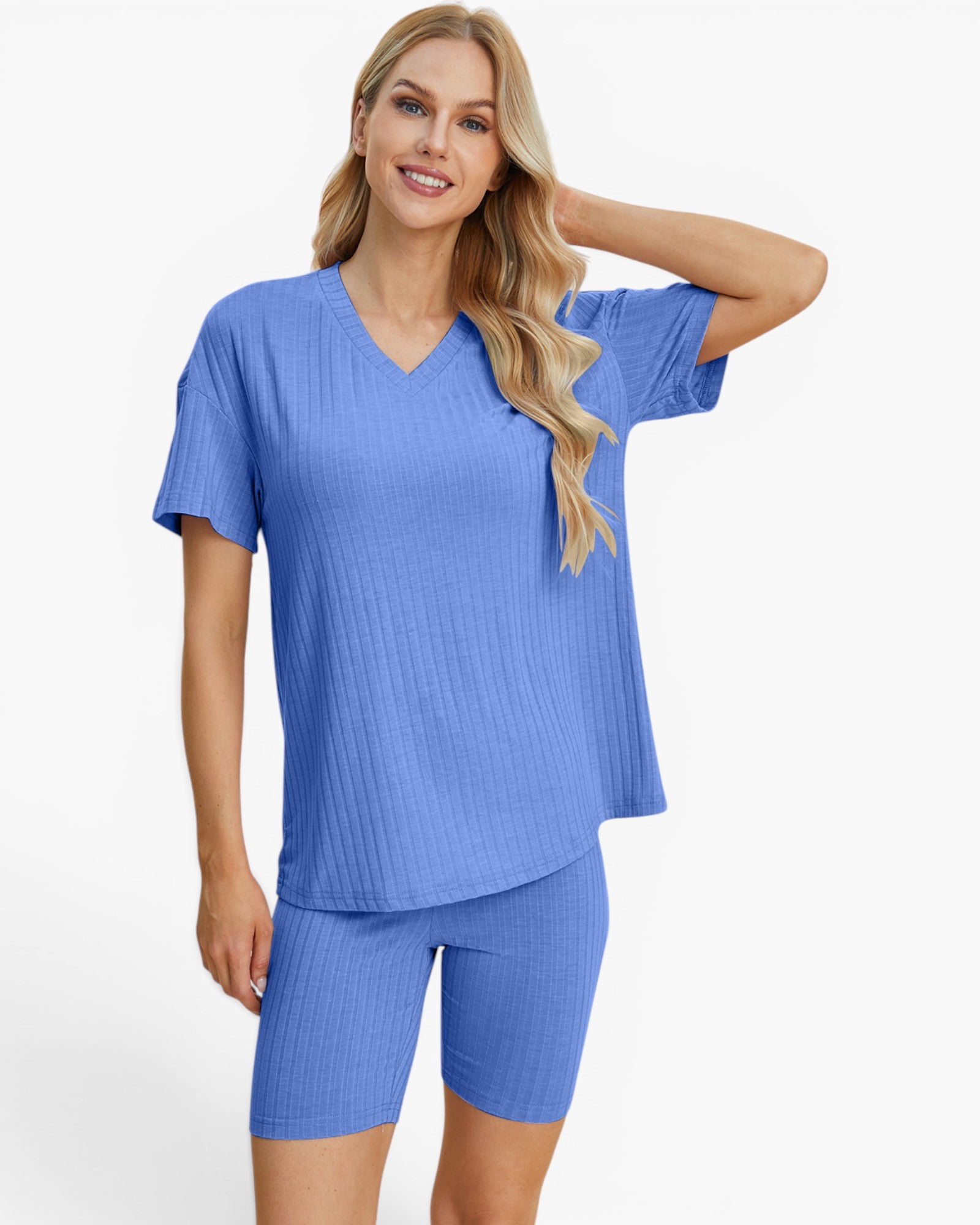 A woman modeling a matching ribbed two-piece loungewear set in a medium periwinkle blue color, consisting of a short-sleeve V-neck top and matching fitted shorts, against a plain white studio background.