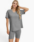 A woman modeling a matching gray ribbed two-piece loungewear set consisting of a short-sleeve V-neck top and fitted biker shorts against a plain white background.