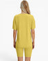 A woman viewed from the back wearing a matching yellow ribbed short-sleeve top and biker shorts set against a plain white background.