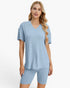 A woman modeling a light blue ribbed short-sleeve V-neck top with matching ribbed biker shorts against a plain white studio background.