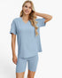 A woman modeling a light blue ribbed short-sleeve V-neck top and matching ribbed biker shorts against a plain white studio background.