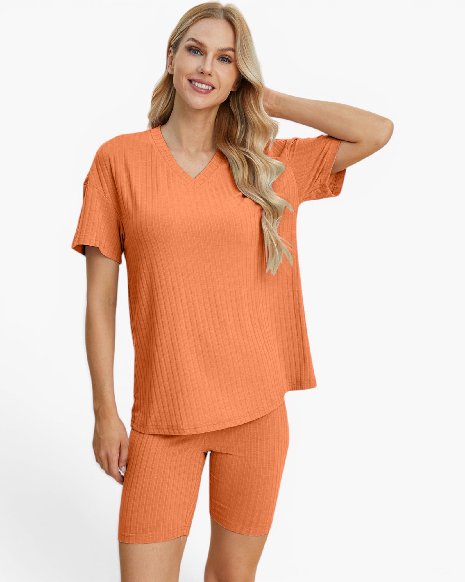 A woman modeling a matching two-piece ribbed knit loungewear set in a warm orange color, featuring a short-sleeve V-neck top and matching biker shorts, against a plain white studio background.