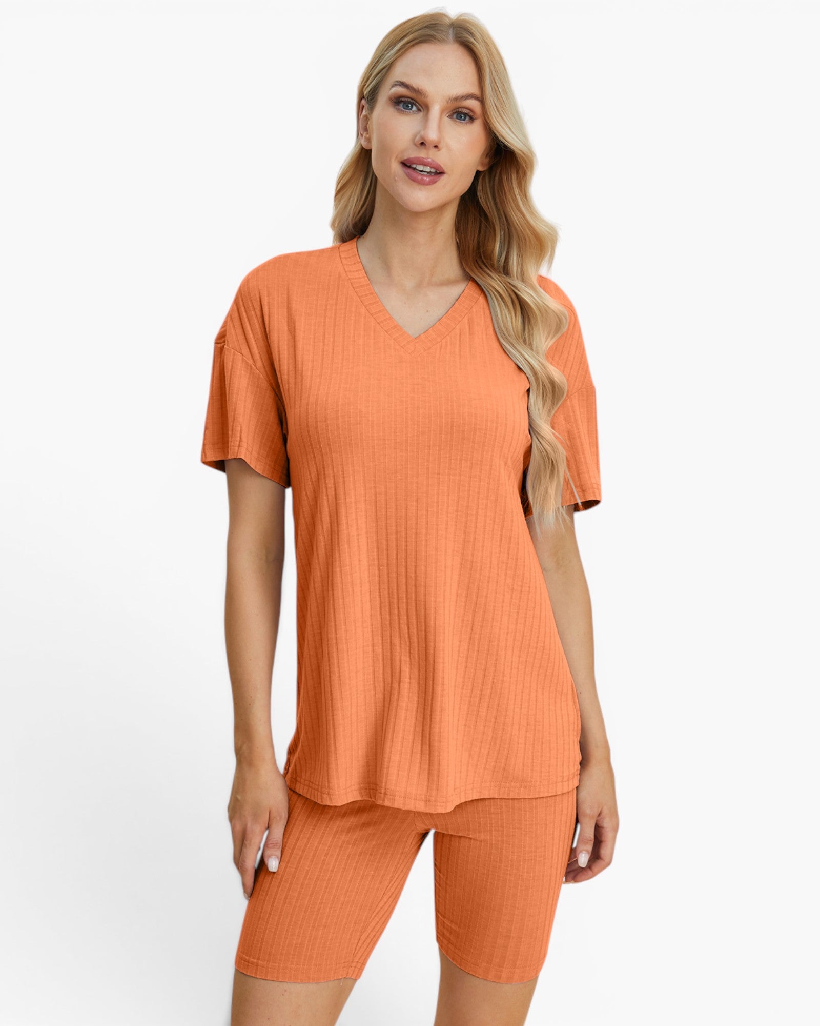 A woman modeling a matching two-piece lounge set consisting of a short-sleeve V-neck ribbed top and matching ribbed biker shorts in a warm orange color, set against a plain white studio background.