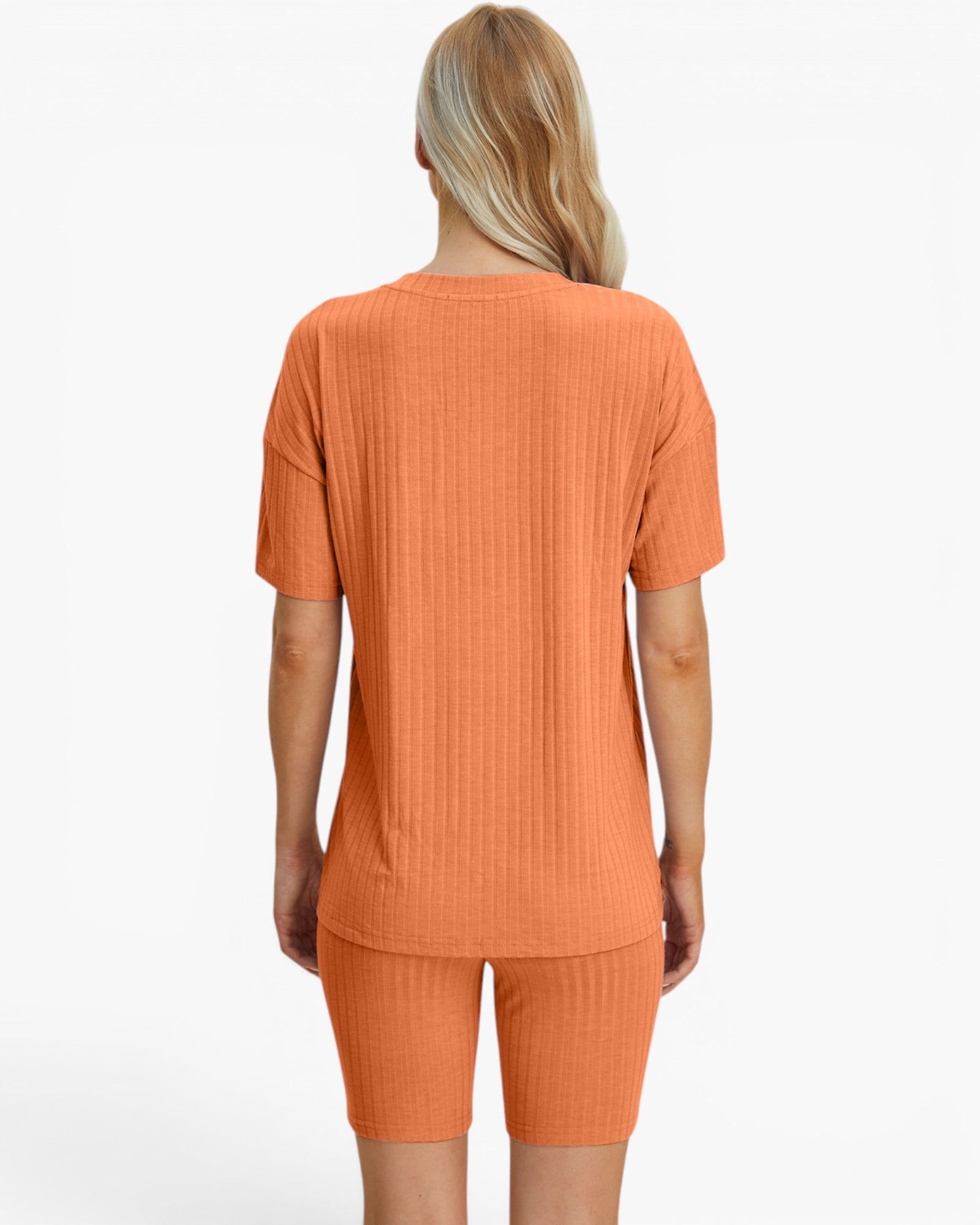 A woman shown from the back wearing a matching ribbed short-sleeve top and biker shorts set in a warm orange color, against a plain white studio background.