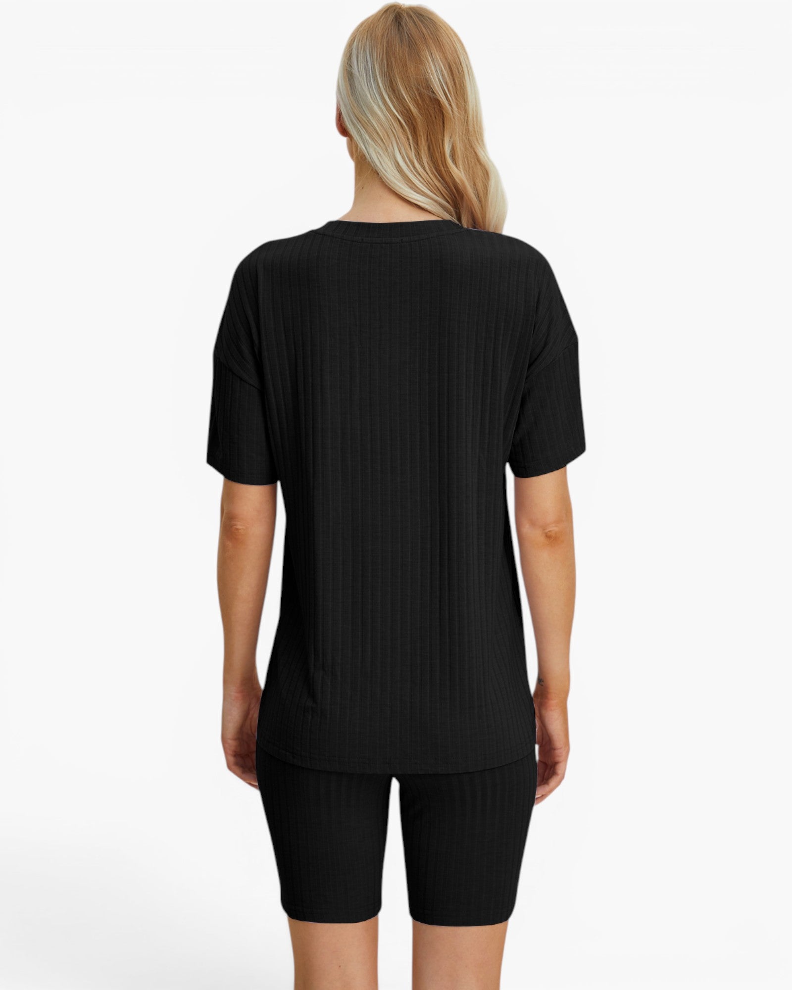 A woman viewed from the back wearing a black short-sleeve ribbed top and matching black ribbed biker shorts against a plain light gray studio background.
