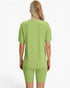 A woman viewed from the back wearing a light green ribbed short-sleeve top and matching ribbed biker shorts against a plain white studio background.