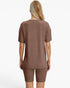 A woman shown from the back wearing a matching ribbed short-sleeve top and biker shorts set in a warm taupe-brown color, against a plain white studio background.