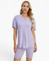 A woman modeling a light purple ribbed short-sleeve V-neck top and matching ribbed biker shorts against a plain white studio background.