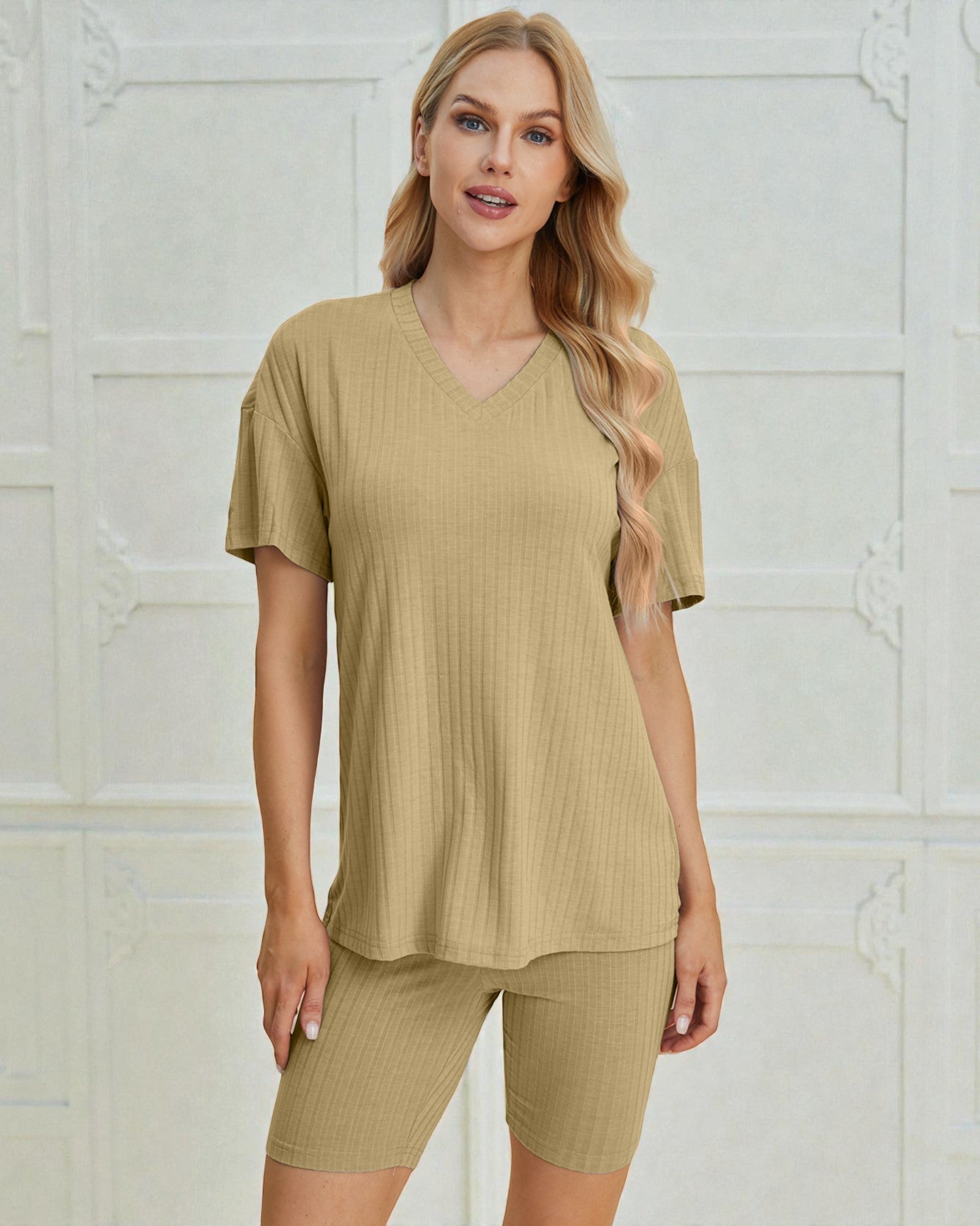Woman wearing a beige ribbed top and shorts set against a light-colored wall.