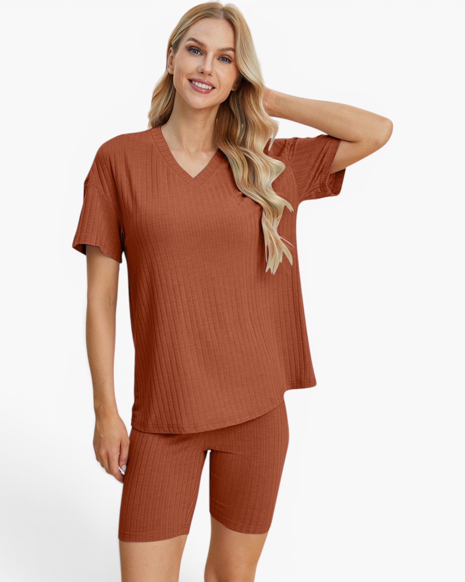 A woman modeling a matching rust-colored ribbed two-piece loungewear set consisting of a short-sleeve V-neck top and fitted biker shorts, against a plain white studio background.