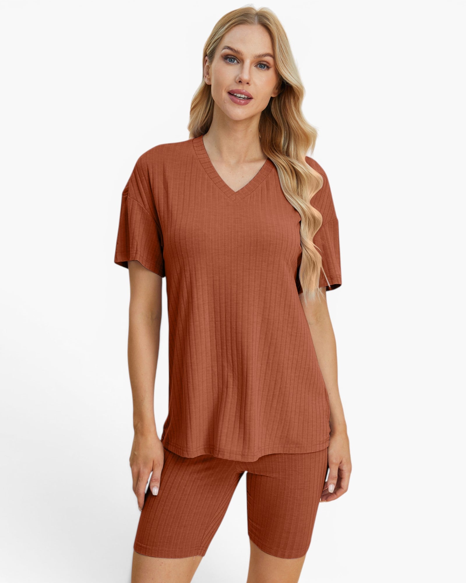 A woman modeling a matching rust-colored ribbed lounge set consisting of a short-sleeve V-neck top and fitted biker shorts, against a plain white studio background.