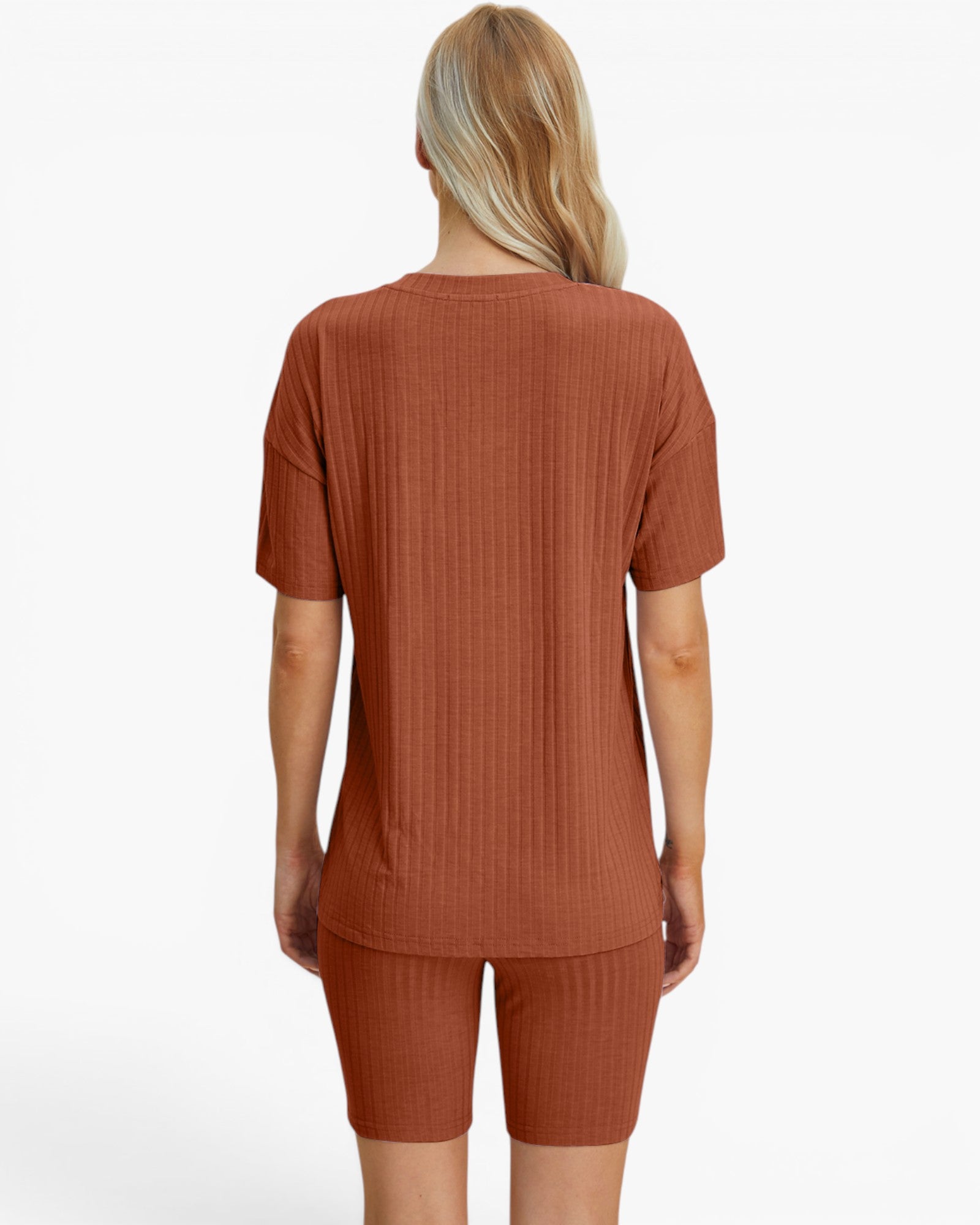A woman viewed from the back wearing a rust-orange ribbed short-sleeve top and matching ribbed biker shorts against a plain light gray studio background.