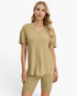 A woman modeling a matching two-piece lounge set consisting of a short-sleeve V-neck ribbed top and matching ribbed biker shorts in a light khaki color, set against a plain white background.