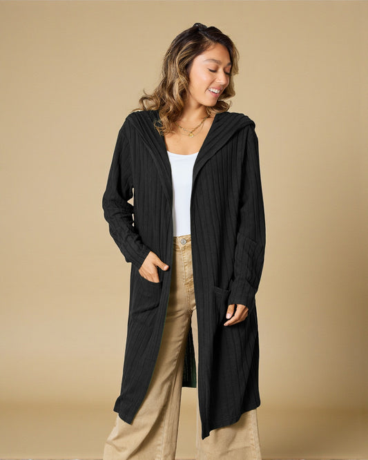 Woman wearing a black long cardigan over a white top and beige pants on a beige background