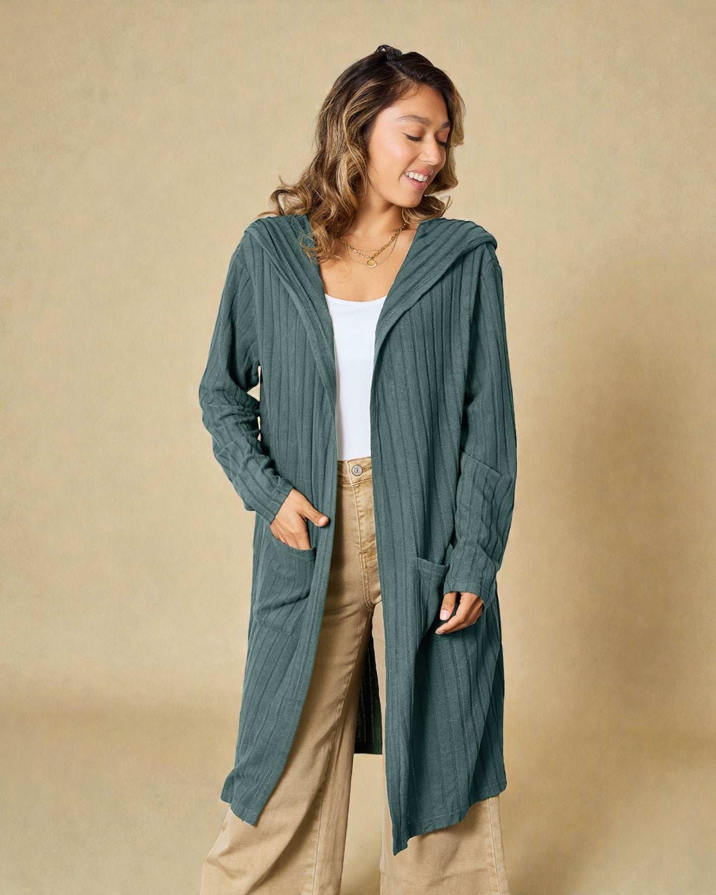 Woman wearing a teal cardigan over a white top and beige pants on a beige background