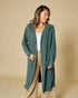Woman wearing a teal cardigan over a white top and beige pants on a beige background
