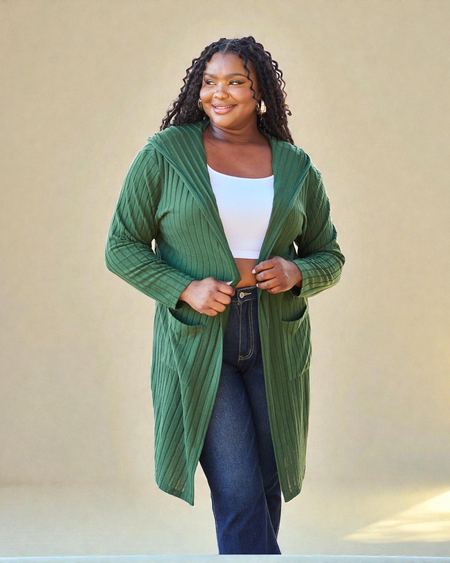 Woman wearing a green cardigan over a white top and jeans against a beige background