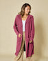 Woman wearing a long pink cardigan over a white top and beige pants on a beige background