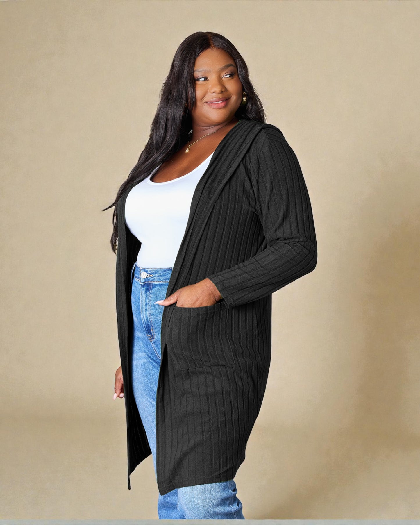 Woman wearing a black cardigan over a white top and blue jeans on a beige background
