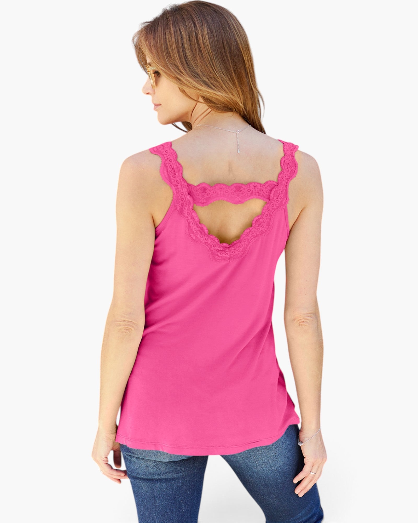 A woman shown from the back wearing a bright pink sleeveless top with a lace-trimmed open back and blue jeans, against a plain light gray studio background.