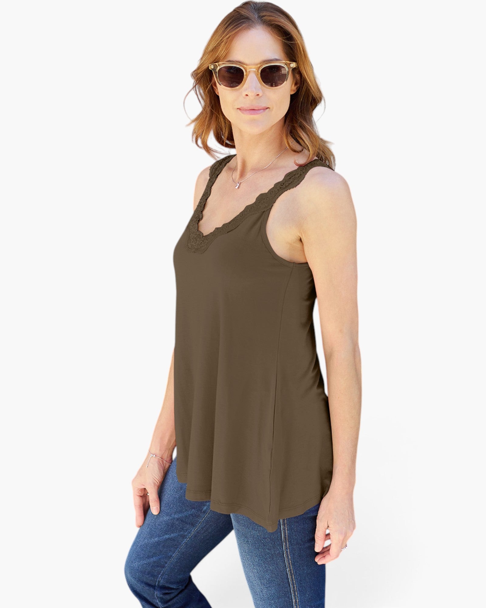 A woman modeling a sleeveless olive brown scoop-neck top with scalloped trim, paired with blue jeans and gold-framed sunglasses, against a plain white background.
