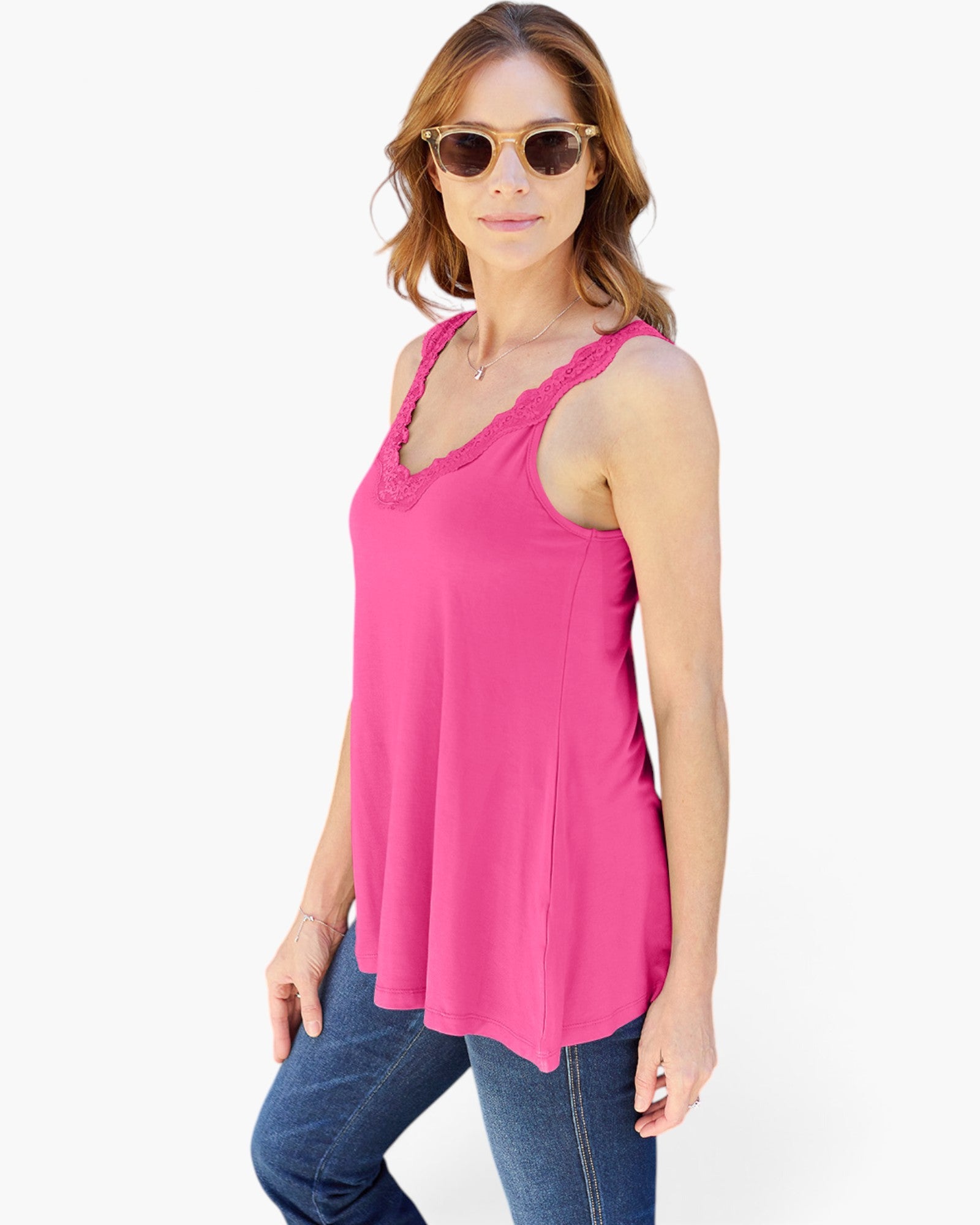 A woman modeling a bright pink sleeveless top with scalloped lace trim at the neckline, paired with blue jeans, against a plain white background.
