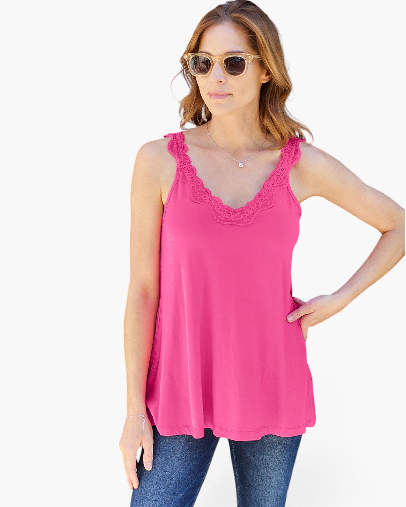 A woman modeling a bright pink sleeveless tank top with a scalloped lace V-neckline, paired with blue jeans against a plain white background.