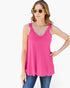 A woman modeling a bright pink sleeveless tank top with a scalloped lace V-neckline, paired with blue jeans against a plain white background.