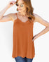 A woman wearing a rust-orange camisole tank top with thin straps and a lace V-neckline, paired with blue jeans and gold-framed sunglasses, against a plain white background.