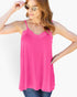 A woman wearing a bright pink sleeveless camisole top with thin straps and a lace V-neckline, paired with blue jeans against a plain white background.