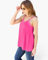 A woman wearing a bright pink camisole top with lace trim and blue jeans, posing against a light gray studio background.