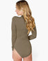 A woman shown from the back wearing a long-sleeve, high-neck, body-skimming bodysuit in a solid taupe-brown color, set against a plain light gray background.