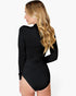 A woman with long blonde wavy hair is shown from the back wearing a black long-sleeve bodysuit with a high neck and a side slit, against a plain white background.